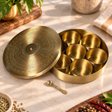 Open brass masala dabba with seven removable compartments and small decorative brass spoon