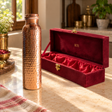 Hammered copper water bottle beside an open maroon satin-lined gift box