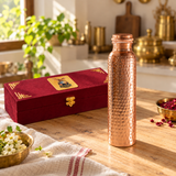 Hammered copper water bottle and closed maroon gift box on a wooden kitchen table