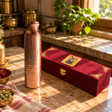 Hammered copper water bottle with its maroon gift box in a sunlit traditional kitchen