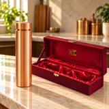 Polished wide-cap copper water bottle beside its open maroon gift box with red satin lining