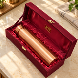 Polished wide-cap copper water bottle resting inside its red satin lined maroon gift box