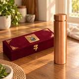 Polished copper water bottle with wide flat cap and closed maroon gift box in natural window light