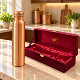 Slim brushed copper water bottle beside its open maroon gift box with red satin lining
