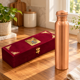 Slim brushed copper water bottle and closed maroon gift box in natural window light