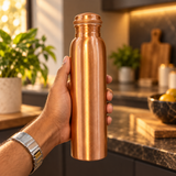 Slim copper water bottle held in hand in a warm kitchen lifestyle scene
