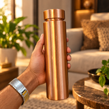 Wide cap copper water bottle held in hand in a warm home lifestyle setting